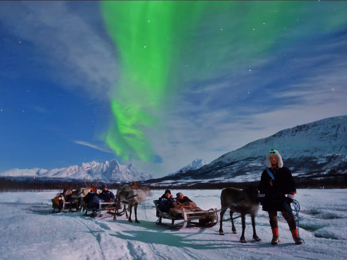Aurora over snowy landscape with travelers in reindeer sleds