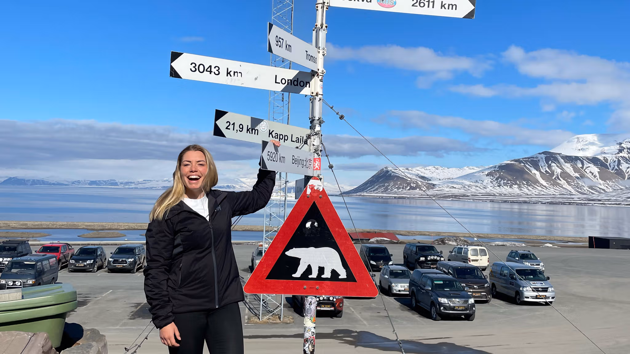 A woman laughing while posing besides the famous polar bear traffic sign at Svalbard
