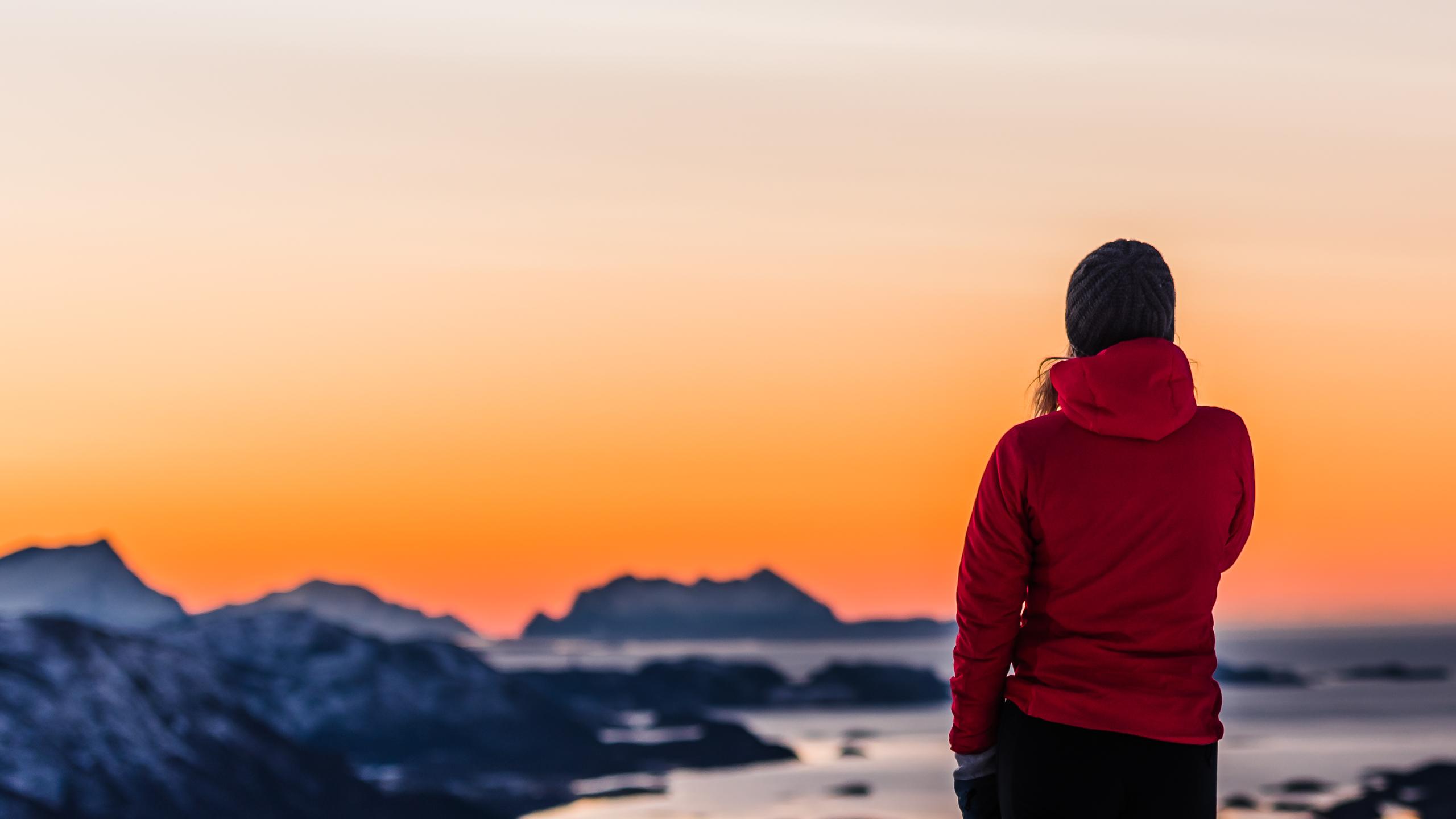 En person ser på utsikten fra en fjelltopp i Bodø med oransje himmel i bakgrunnen.