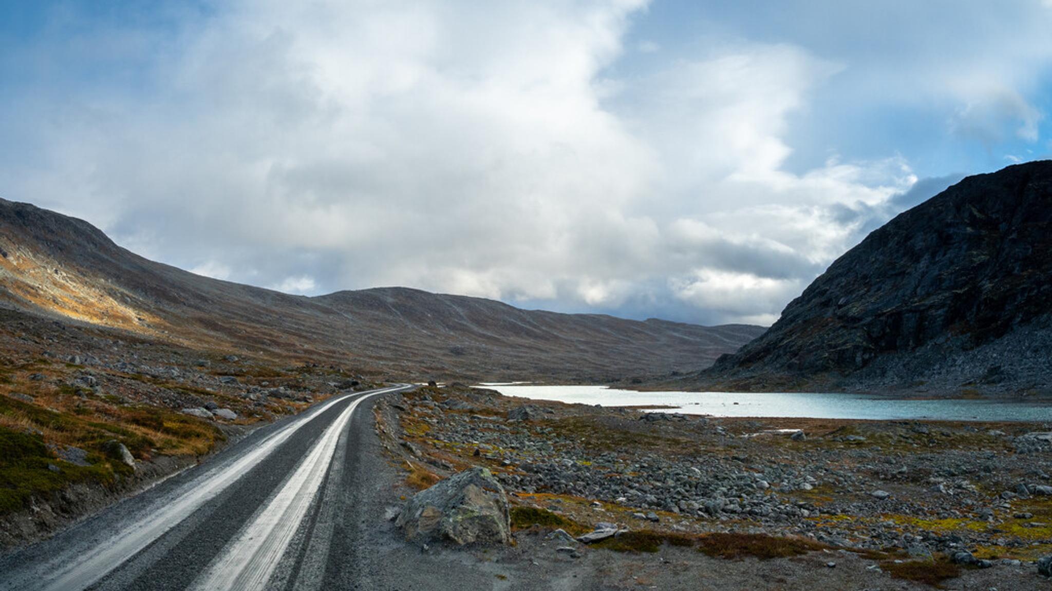 A road high up in the mountains next to a lake.