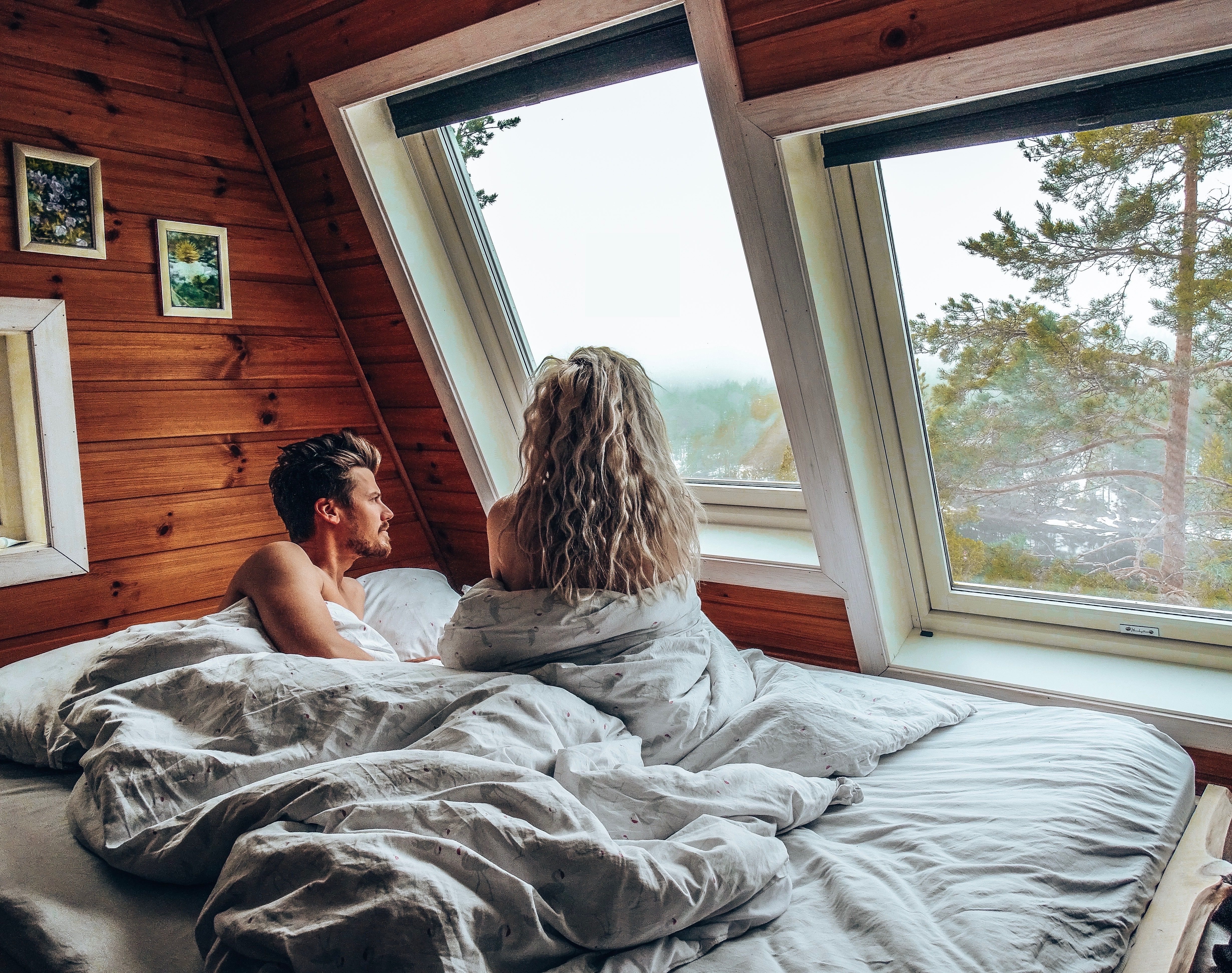 En dame og en mann sitter i sengen og ser ut av vinduet på Mikrohyttene i Kragerø i Telemark, Østlandet