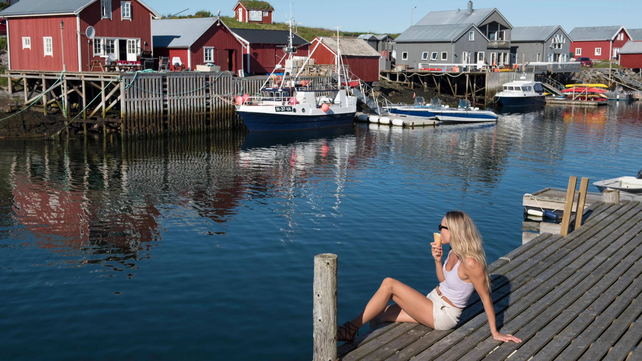 A woman sitting and eating an ice cream by the harbour on Vega in Helgeland, Northern Norway.