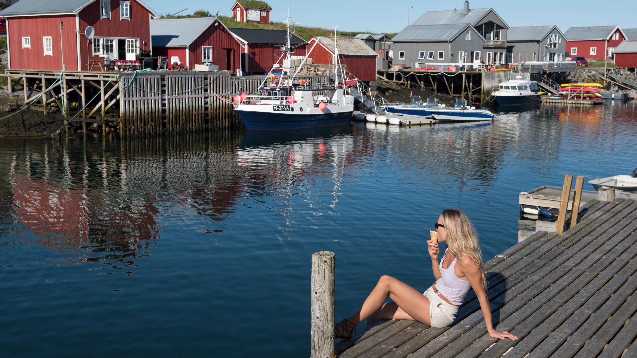 En dame sitter og spiser is i havna på Vega på Helgelandskysten
