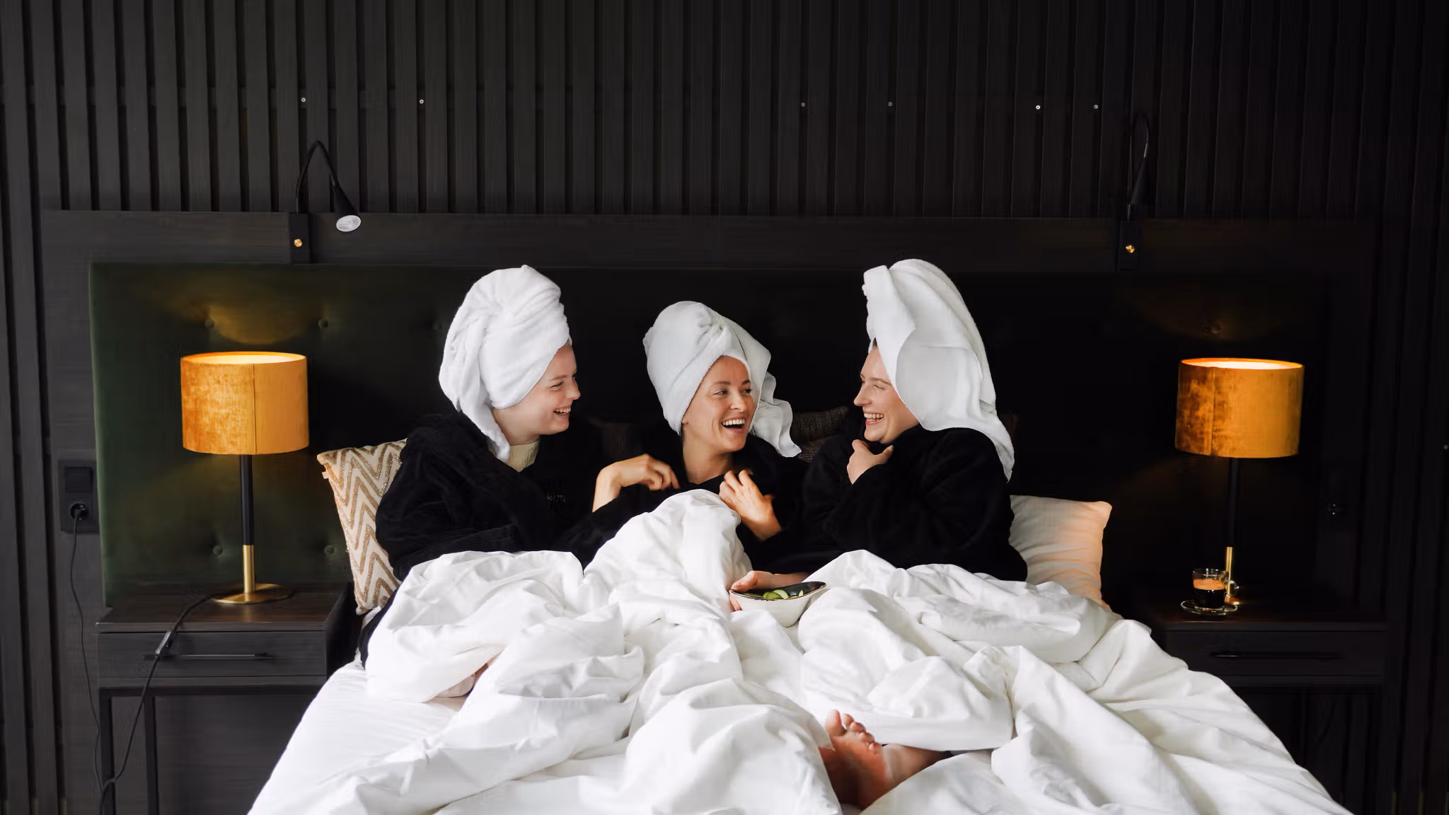 Three girls in a hotel bed smiling.