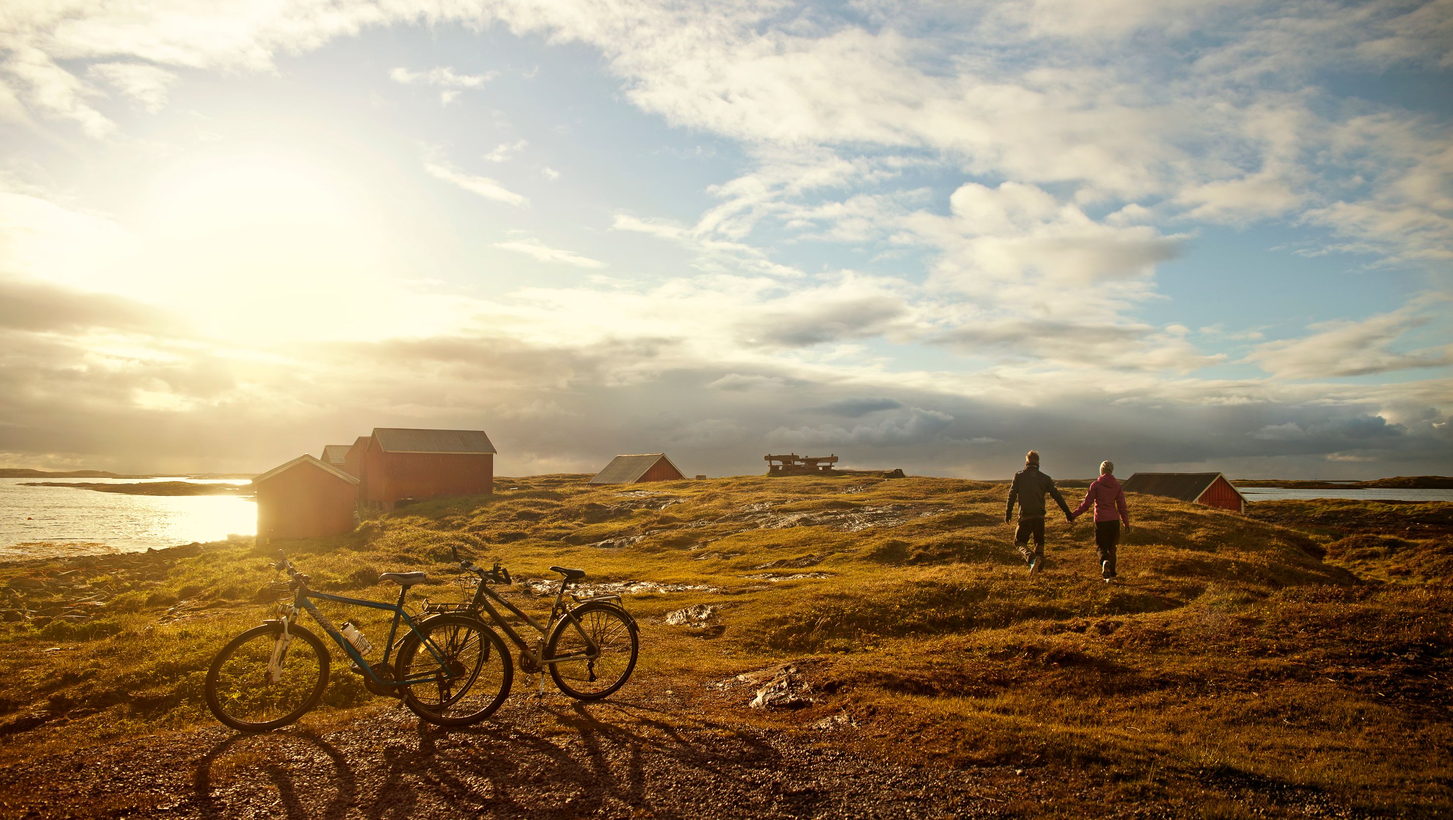 Two people have parked their bikes and are walking towards the sea while the sun is setting at Vega island, Northern Norway