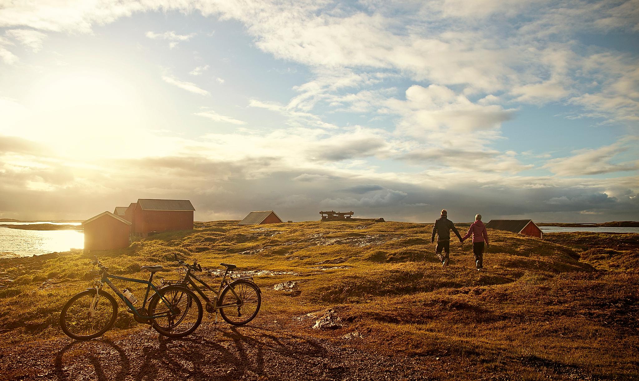 Two people have parked their bikes and are walking towards the sea while the sun is setting at Vega island, Northern Norway