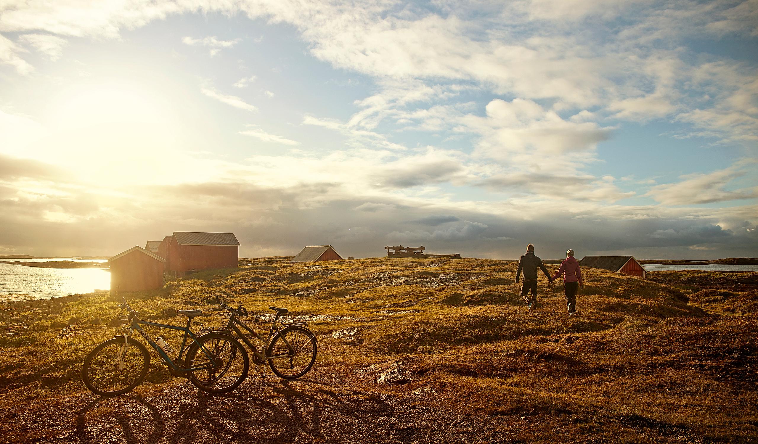 Two people have parked their bikes and are walking towards the sea while the sun is setting at Vega island, Northern Norway