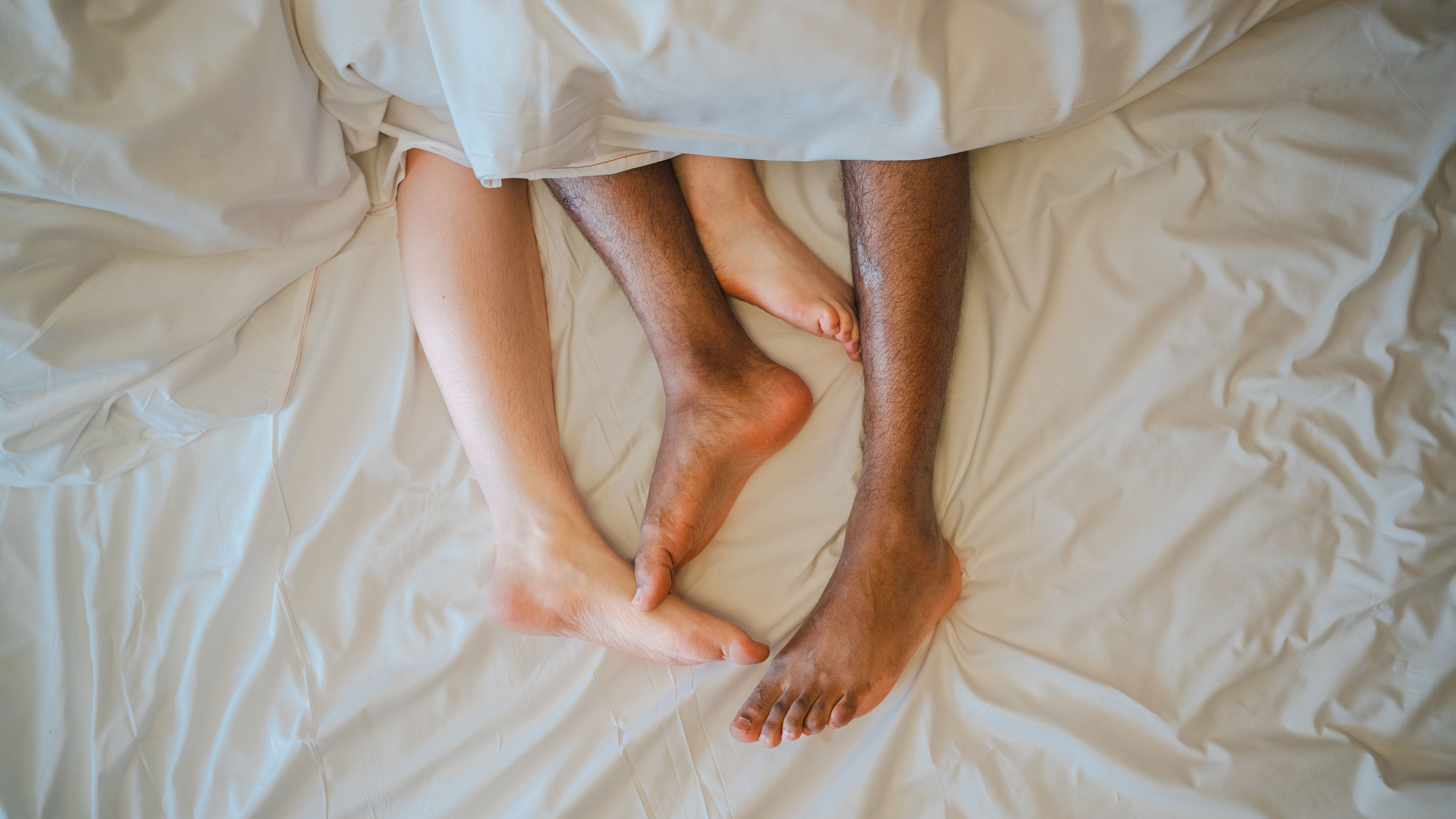 Two feet coming out of a blanket in bed.