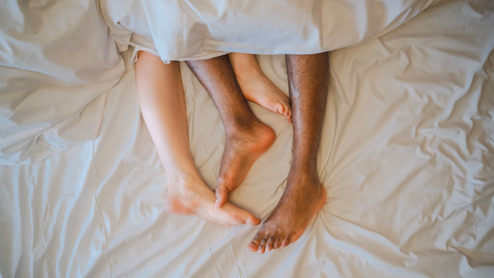 Two feet coming out of a blanket in bed.