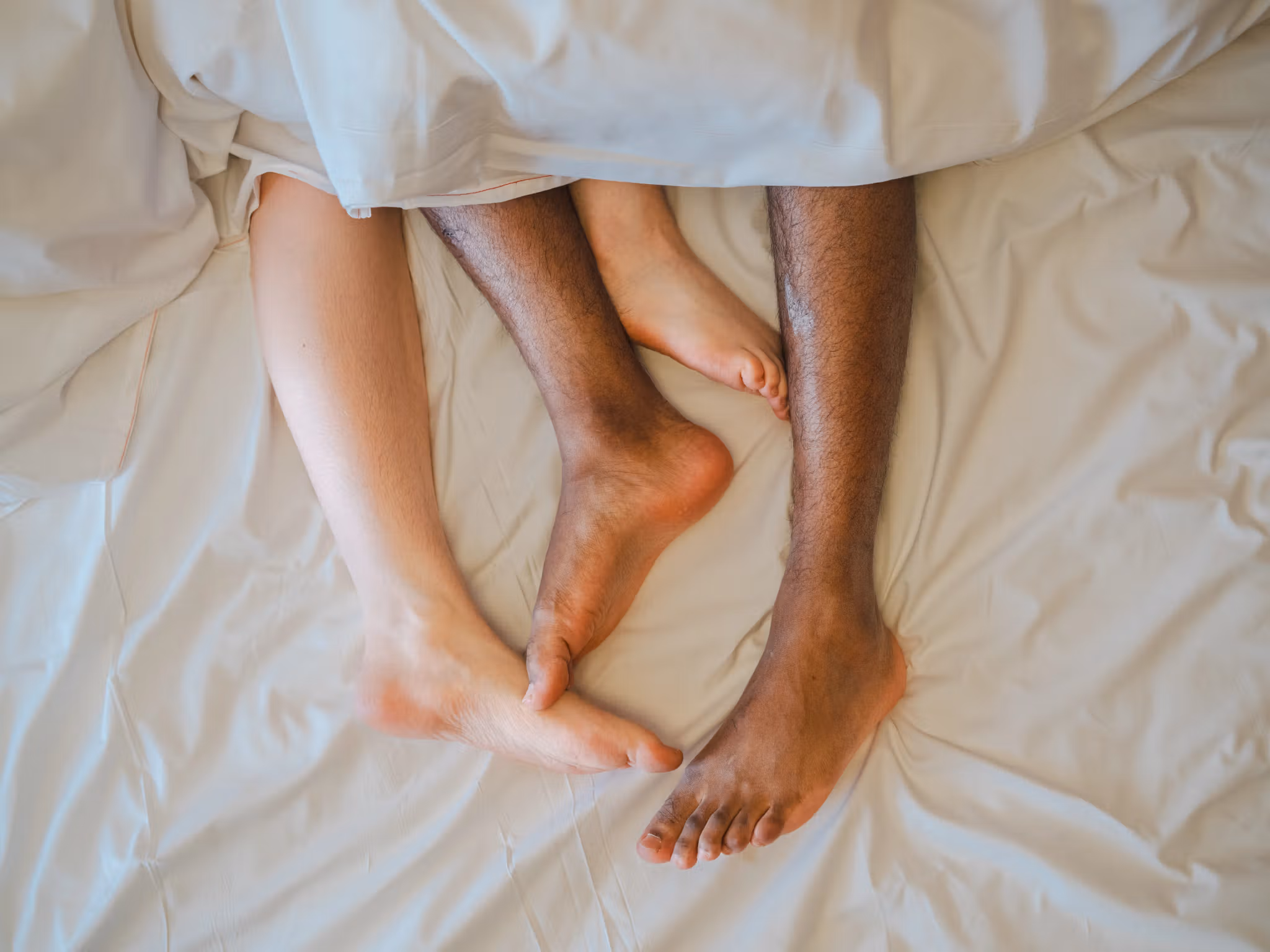 Two feet coming out of a blanket in bed.