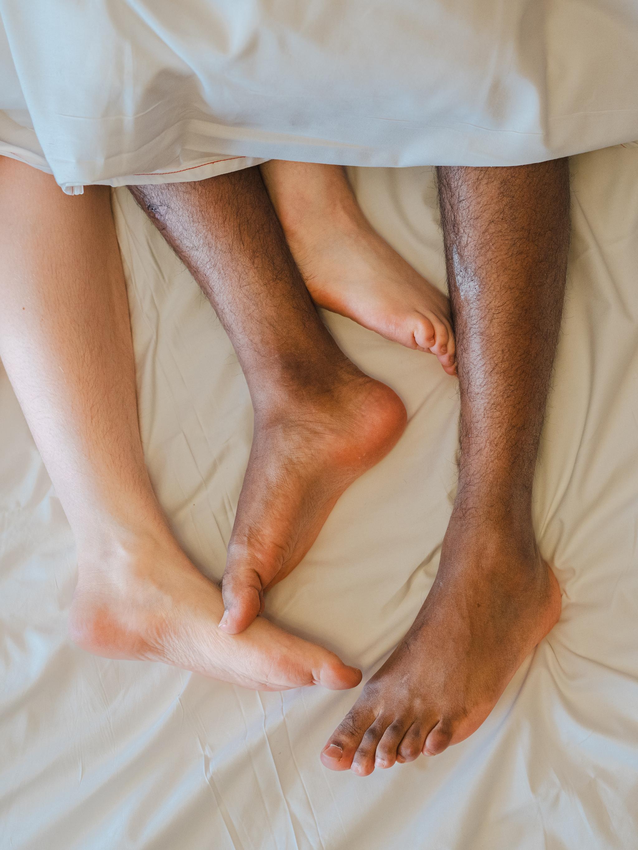 Two feet coming out of a blanket in bed.