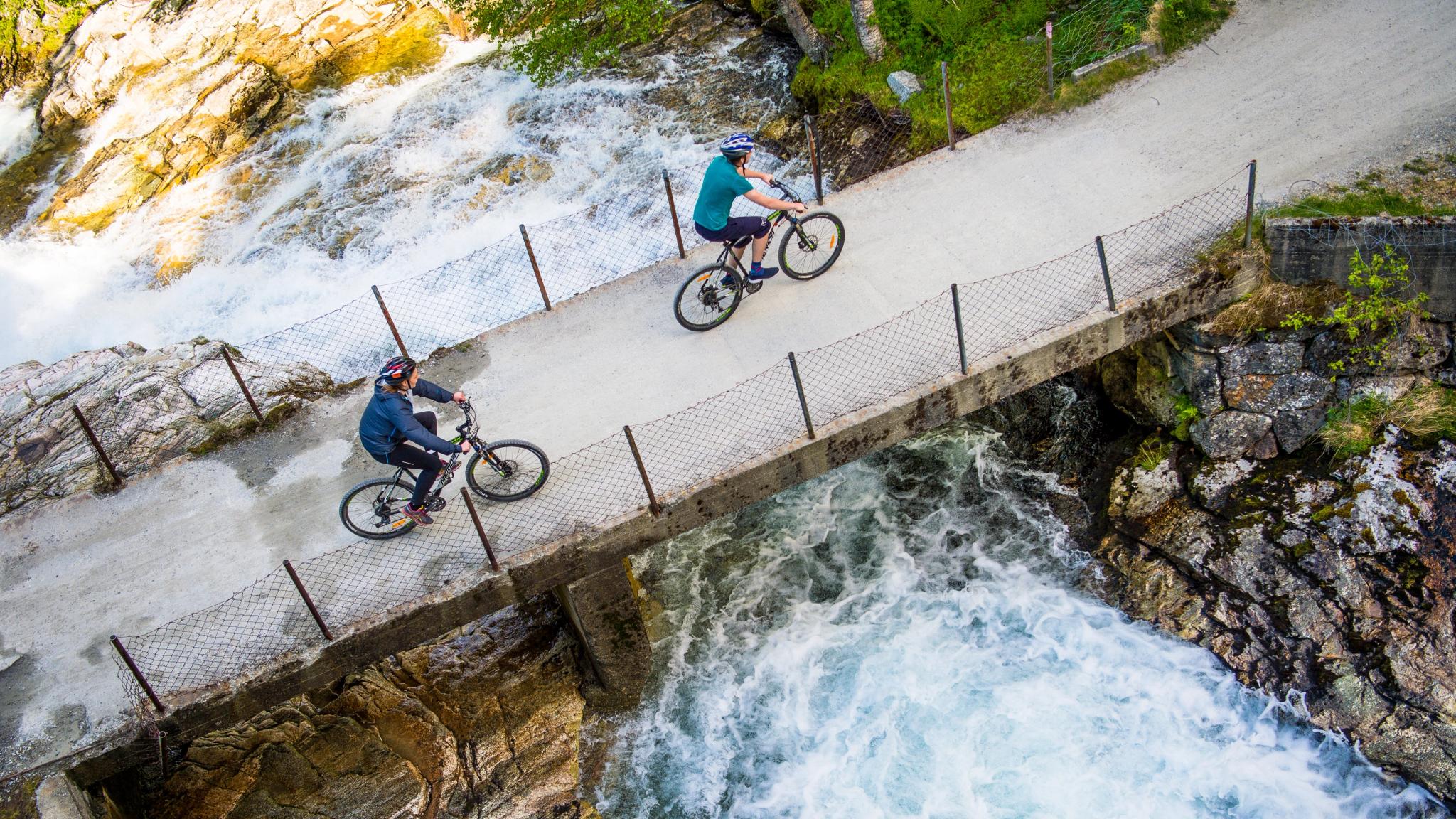 Two cyclists crossing a bridge on the river on the Rallarvegen, Fjord Norway