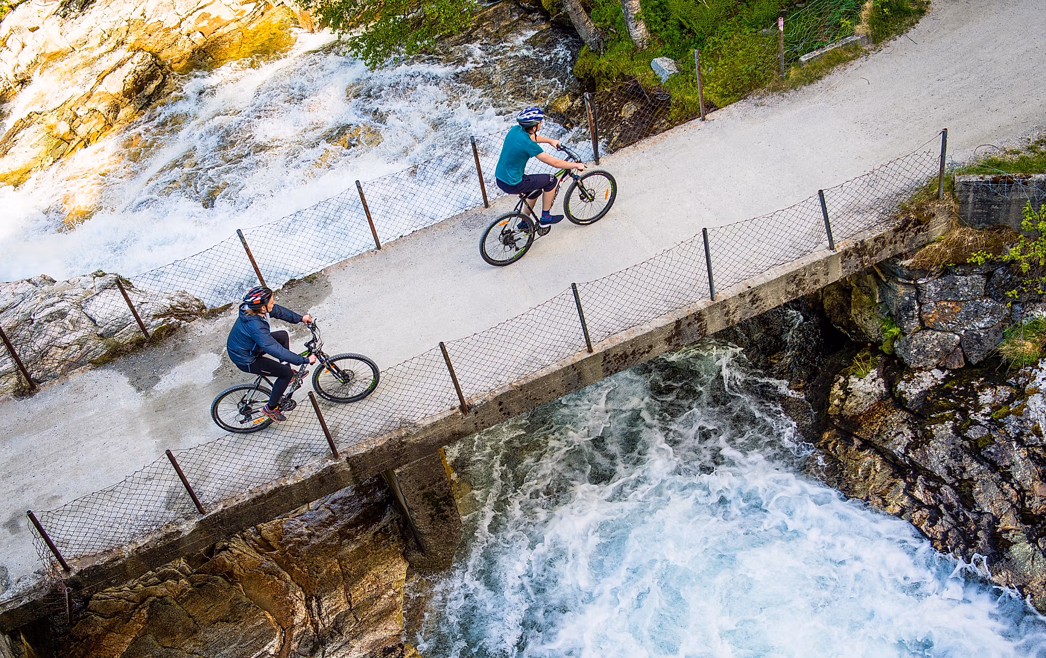 Two cyclists crossing a bridge on the river on the Rallarvegen, Fjord Norway