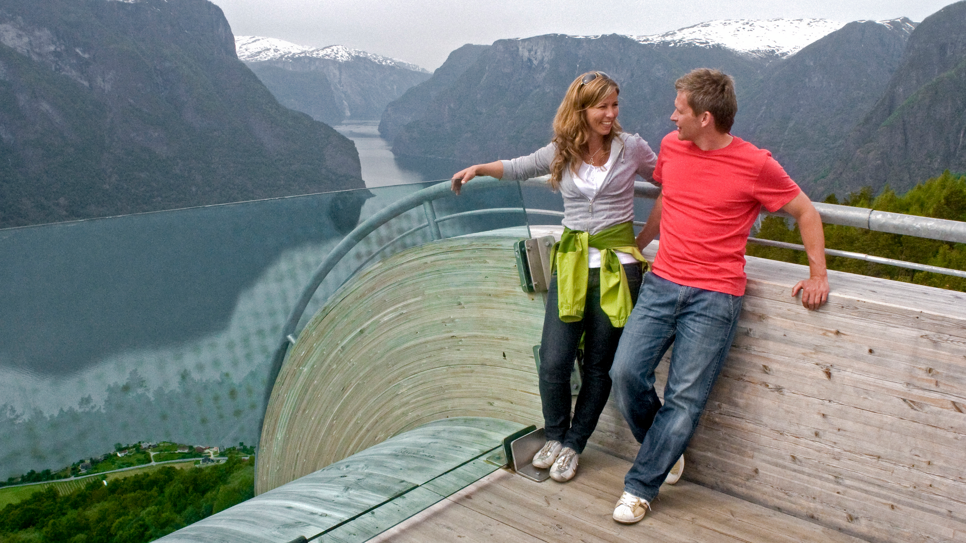 Two people holding each other at a viewpoint overlooking the fjord and mountains