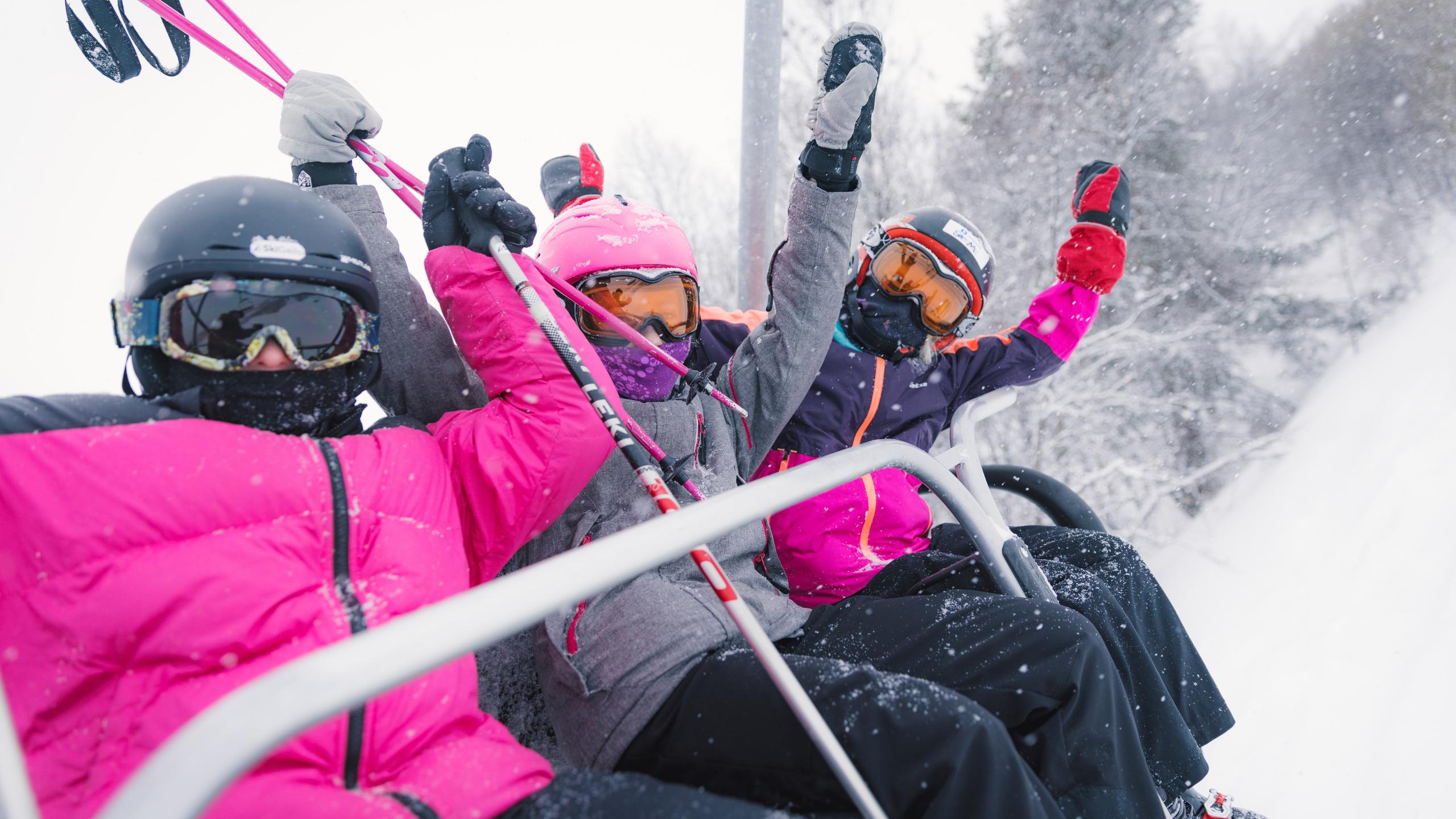 Tre glade jenter sitter i skiheisen på Geilo skisenter, Østlandet, Norge.