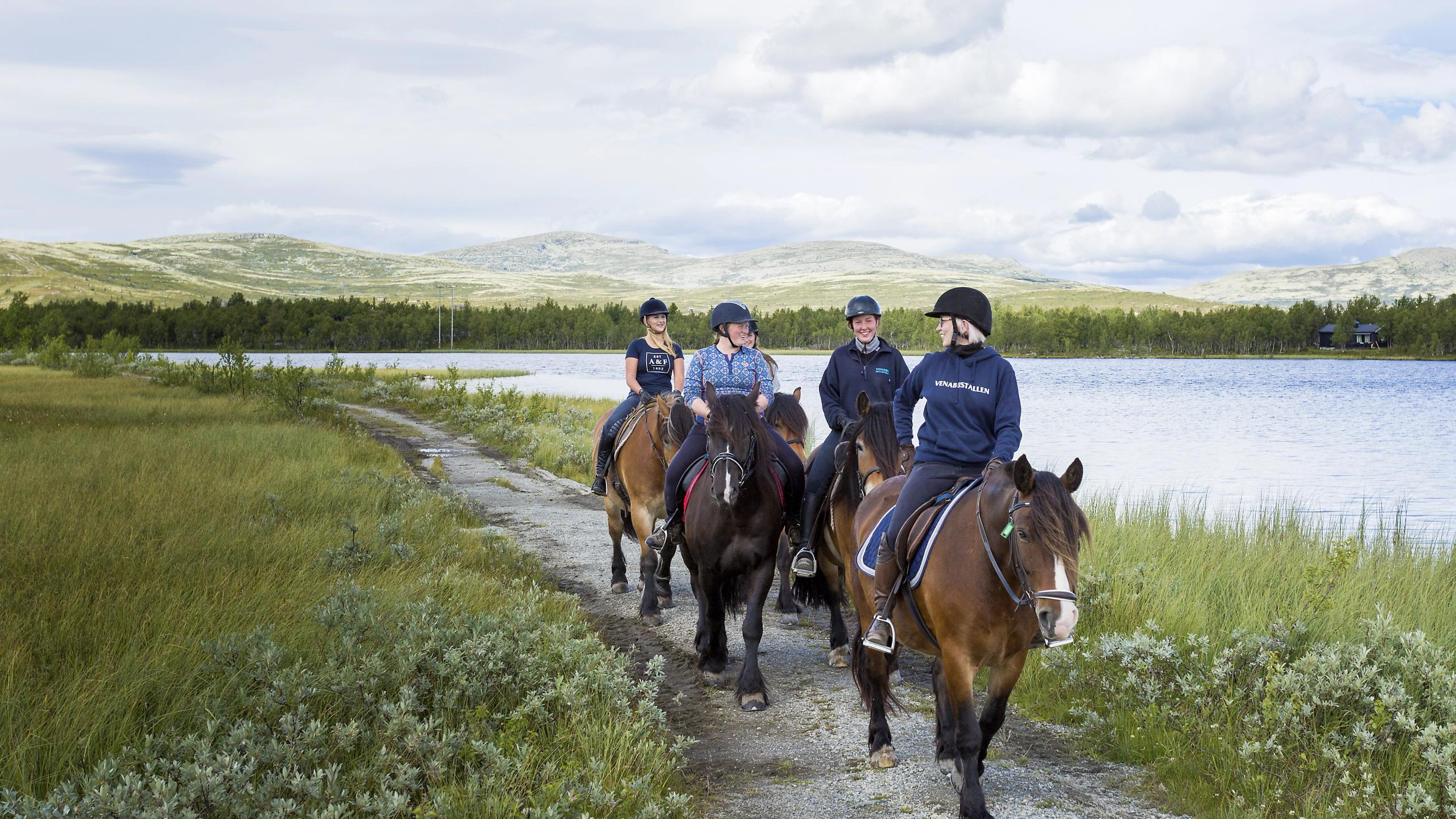 Four women riding horses by a lake
