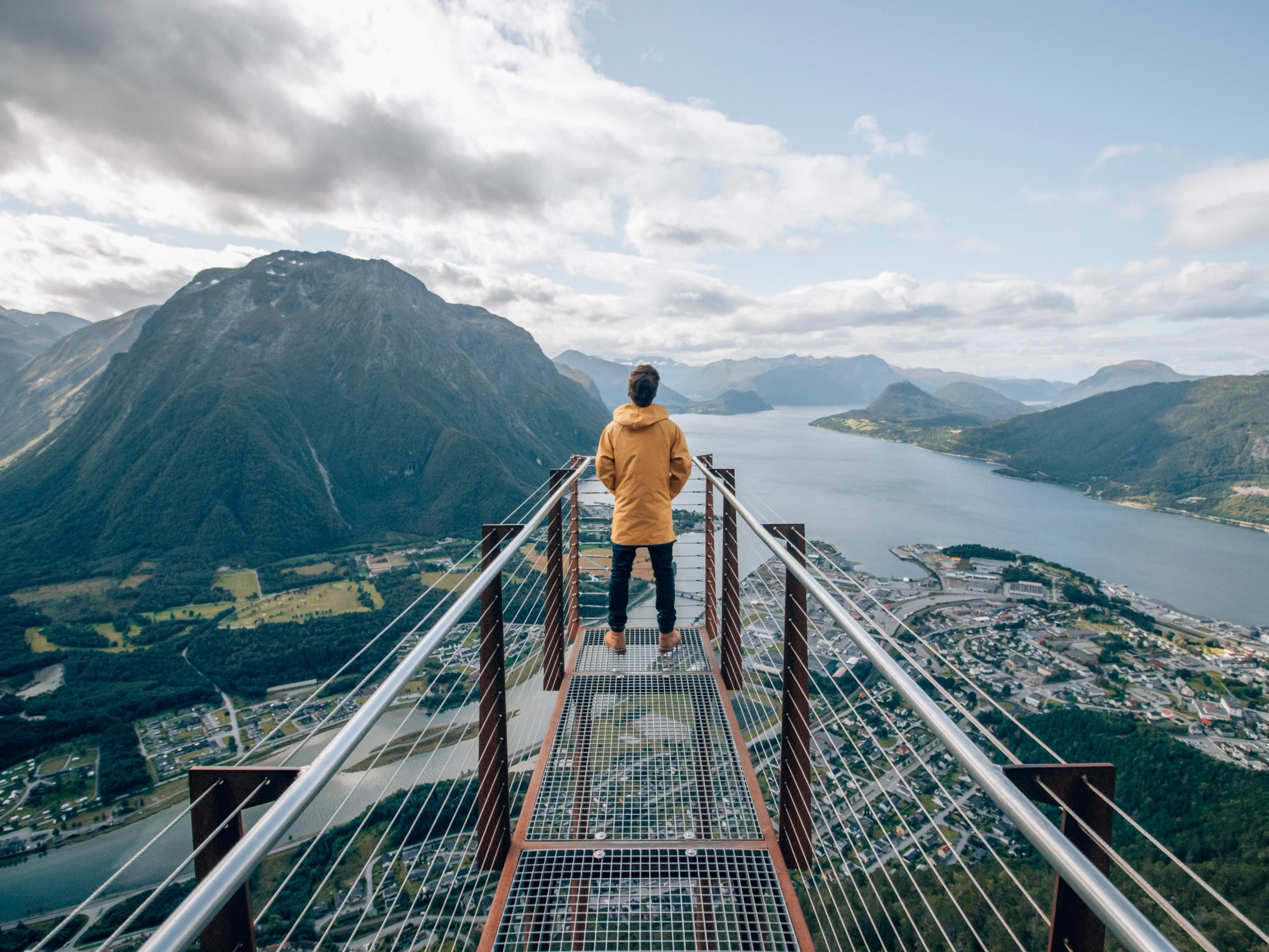 Una persona sulla punta della piattaforma panoramica Rampestreken osserva il fiordo e le montagne di Åndalsnes nel Nordovest dei fiordi, Norvegia dei fiordi