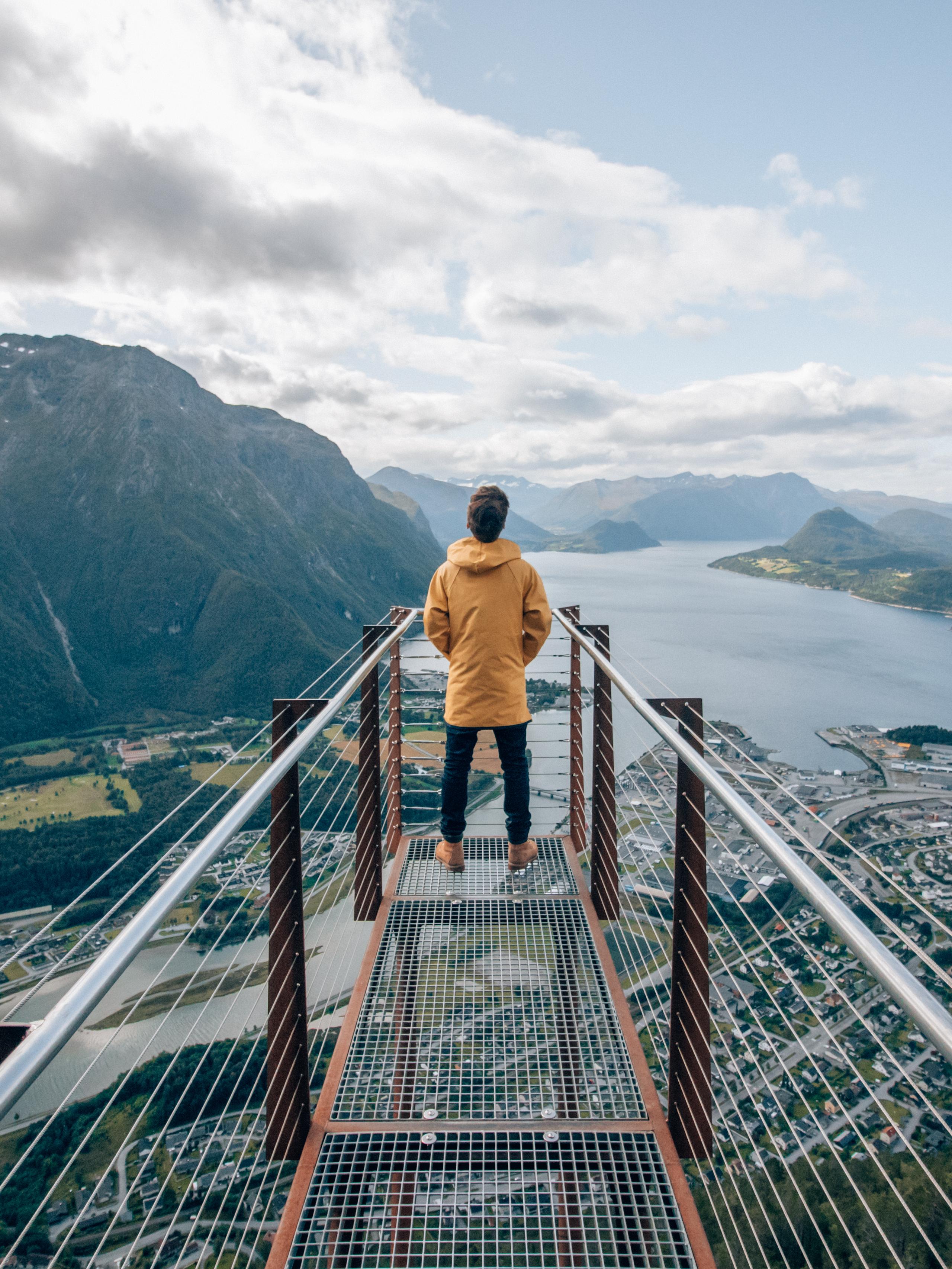 A person standing at the tip of Rampestreken viewpoint, looking out at the fjord and mountains of Åndalsnes in Northwest, Fjord Norway.