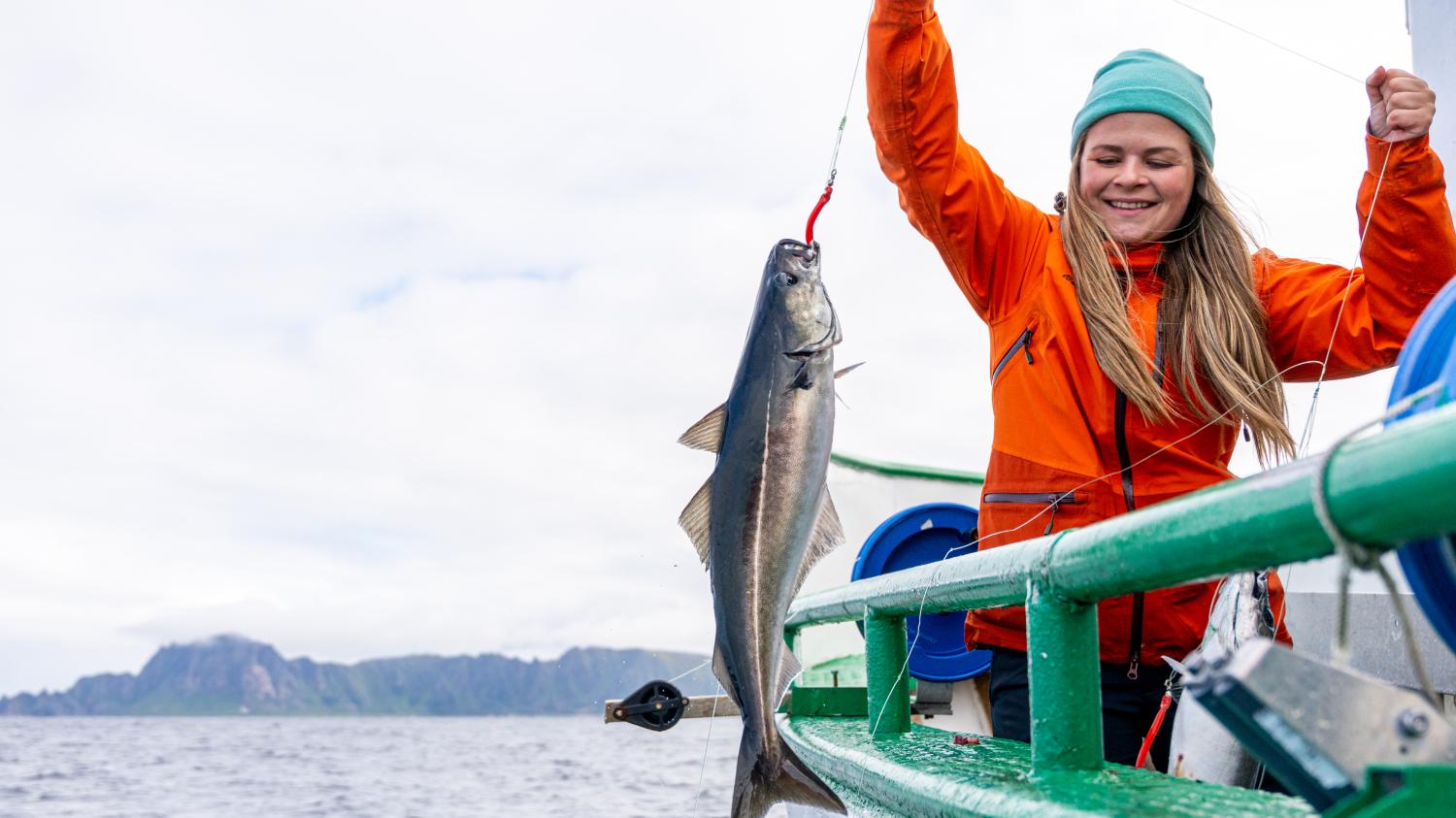 En kvinne drar opp en fisk i en båt.