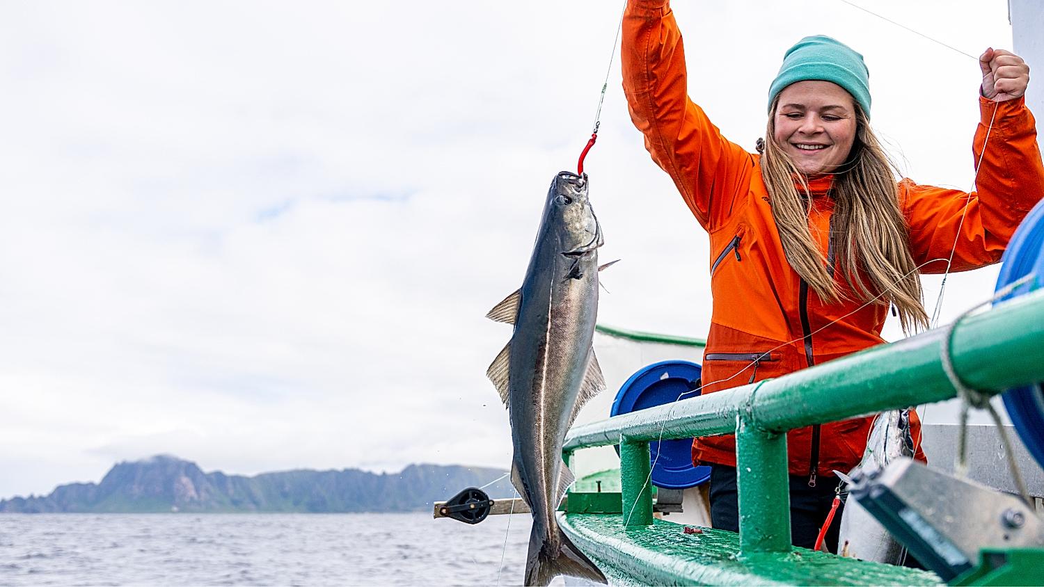 En kvinne drar opp en fisk i en båt.
