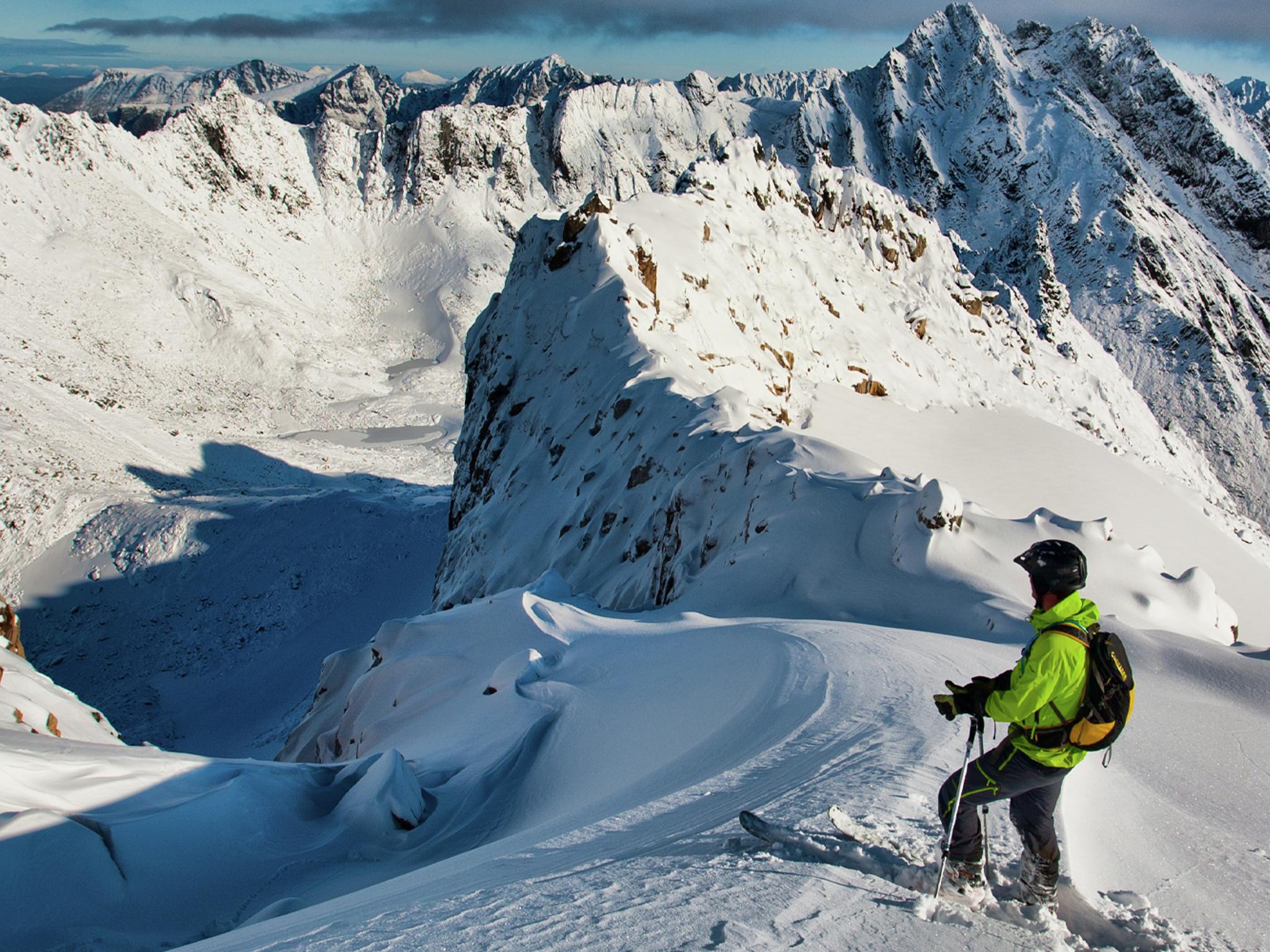 En mann på topptur på ski står klar til å kjøre nedover fjellet